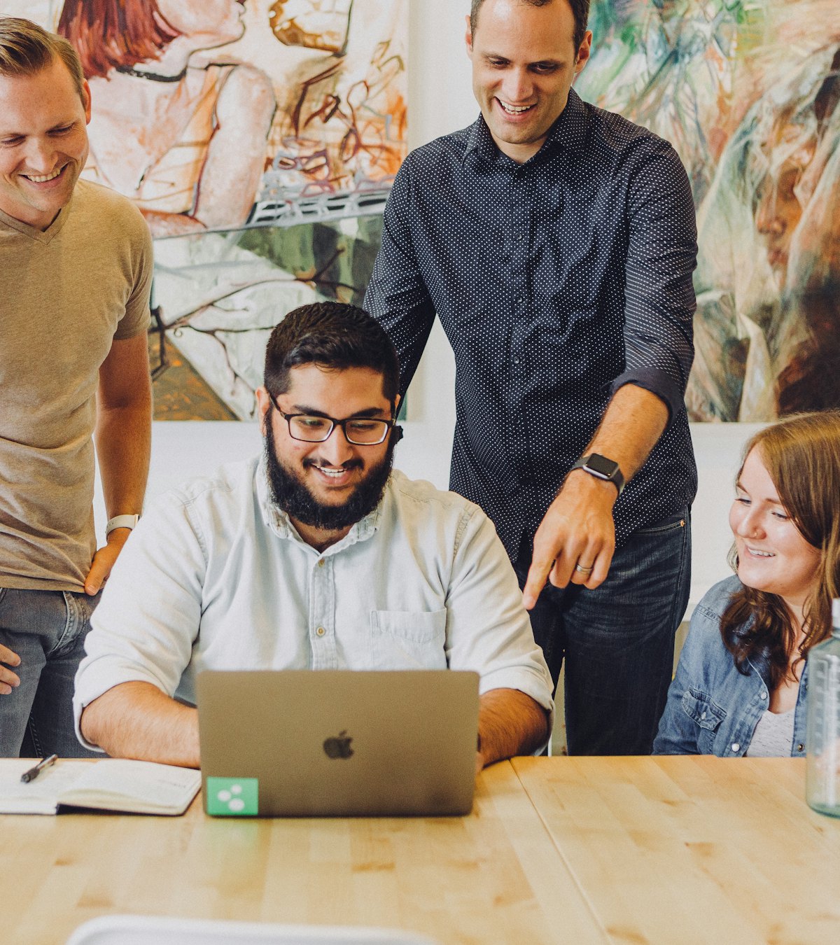 Four colleagues smiling together around a laptop